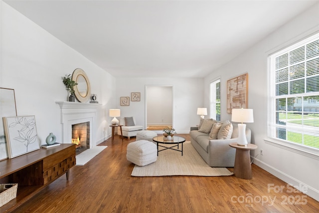 living area with a warm lit fireplace, wood finished floors, and baseboards