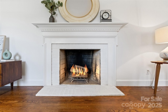 detailed view of baseboards, wood finished floors, and a brick fireplace