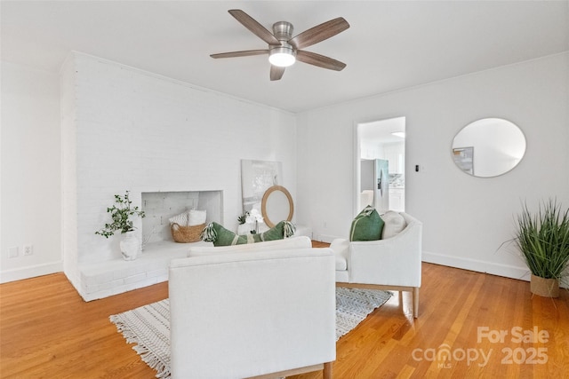 living area featuring ceiling fan, light wood-type flooring, baseboards, and a brick fireplace