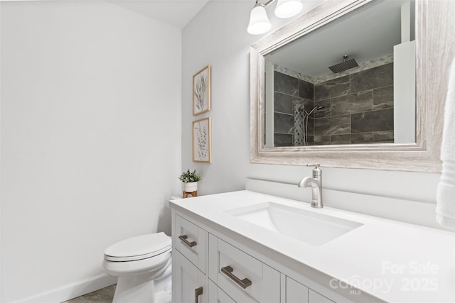 bathroom with vanity, tiled shower, toilet, and baseboards