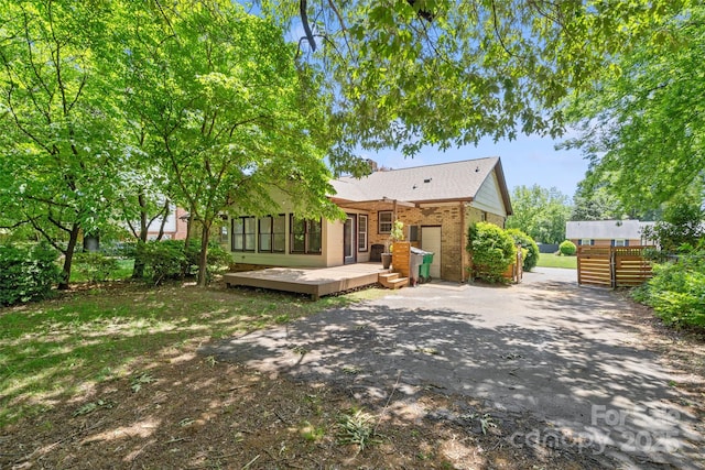 back of house with brick siding, a wooden deck, and asphalt driveway