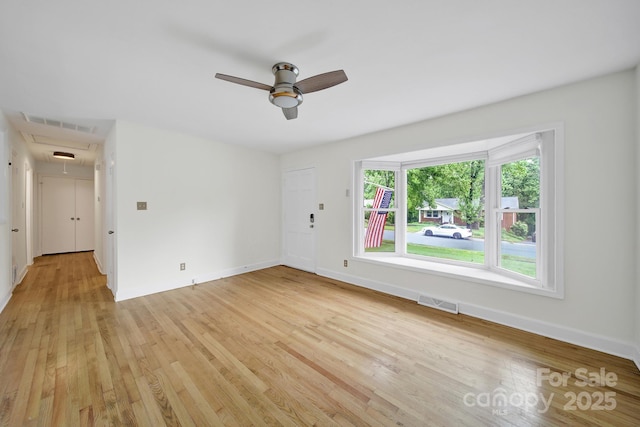 spare room featuring attic access, a ceiling fan, light wood-type flooring, and baseboards
