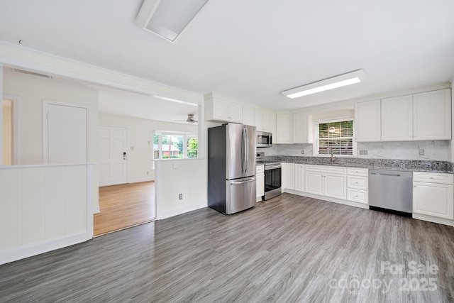 kitchen with appliances with stainless steel finishes, a sink, light wood-style floors, and decorative backsplash