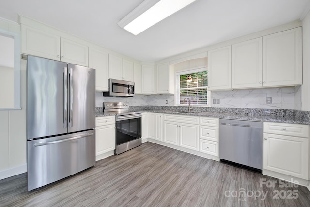 kitchen with stainless steel appliances, white cabinetry, a sink, and light wood-style flooring