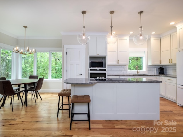 kitchen with appliances with stainless steel finishes, crown molding, a kitchen island, tasteful backsplash, and white cabinets