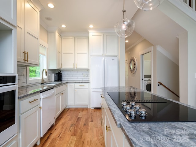 kitchen with white appliances, a sink, light wood finished floors, ornamental molding, and dark stone countertops