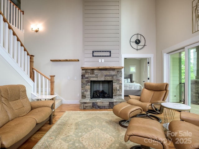 living room featuring a high ceiling, stairway, wood finished floors, a stone fireplace, and baseboards