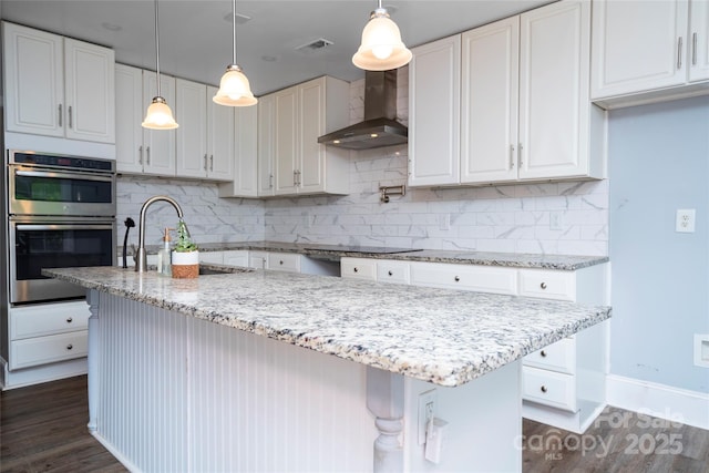 kitchen featuring wall chimney range hood, stainless steel double oven, dark wood finished floors, baseboards, and white cabinetry