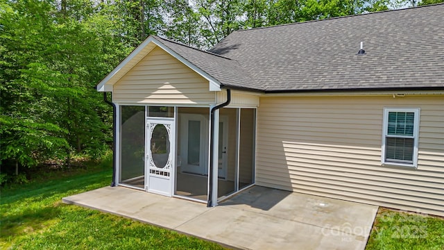 back of house with a sunroom, a patio area, a shingled roof, and a lawn