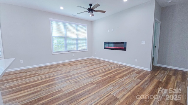 unfurnished living room with wood finished floors, a glass covered fireplace, recessed lighting, ceiling fan, and baseboards