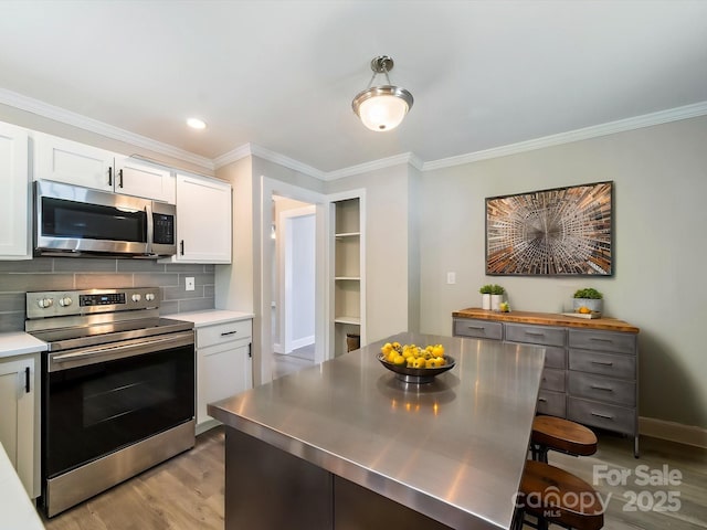 83 Woodsdale Pl SE, Concord, NC 28025 - kitchen with appliances with stainless steel finishes, stainless steel counters, light wood-type flooring, ornamental molding, and white cabinetry