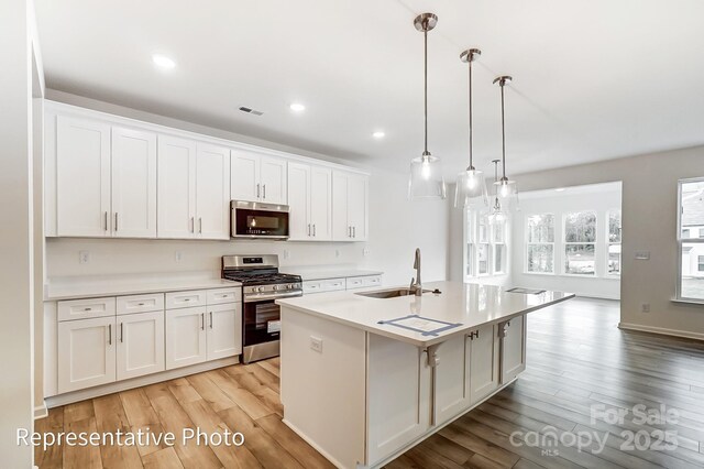 8619 Frank Grier Rd Unit 3, Charlotte, NC 28215 - kitchen featuring appliances with stainless steel finishes, a sink, light wood-type flooring, a kitchen island with sink, and white cabinetry