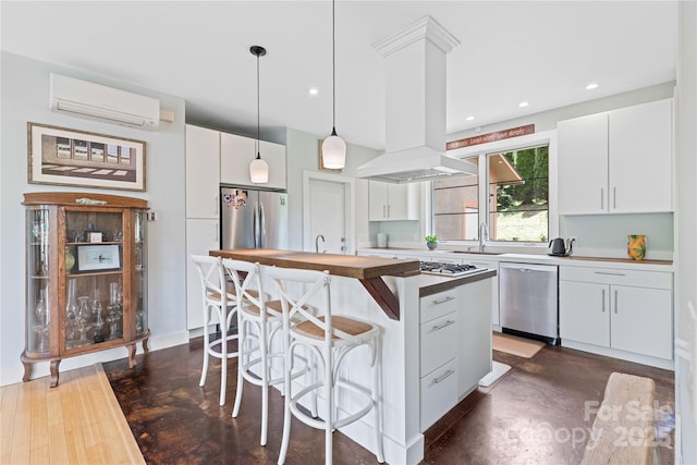 kitchen featuring appliances with stainless steel finishes, a wall mounted AC, island range hood, hanging light fixtures, and a center island with sink