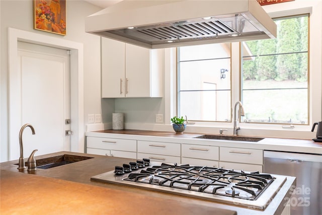 kitchen with ventilation hood, a sink, dishwashing machine, stainless steel gas stovetop, and white cabinetry