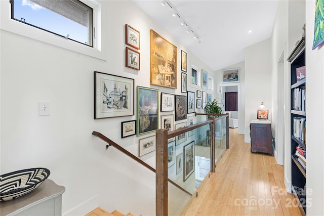 hall featuring an upstairs landing, track lighting, light wood-style floors, lofted ceiling, and baseboards