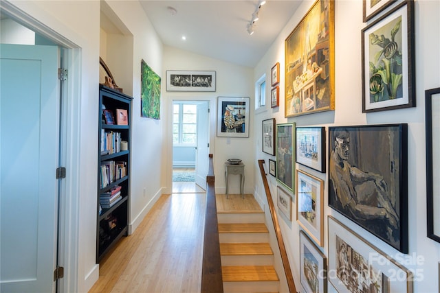 corridor featuring light wood finished floors, vaulted ceiling, and baseboards