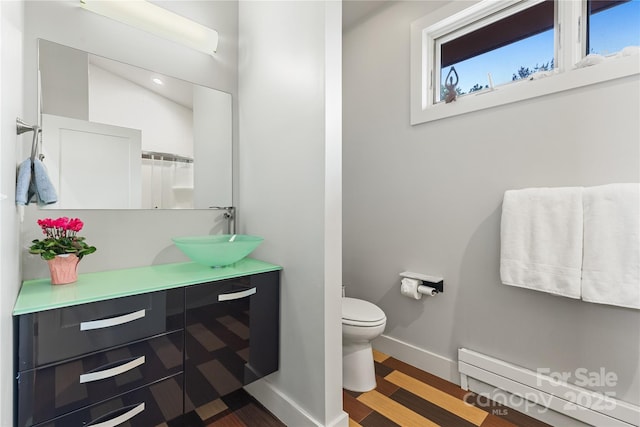 bathroom featuring baseboard heating, wood finished floors, toilet, and vanity