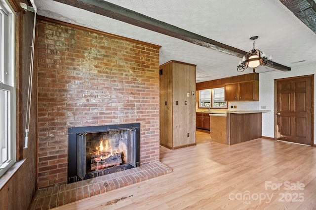 1 Ola Dr, Candler, NC 28715 - kitchen featuring a textured ceiling, light wood finished floors, brown cabinetry, a fireplace, and a peninsula