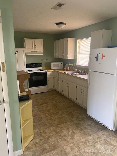 kitchen featuring white appliances, a sink, under cabinet range hood, and light countertops