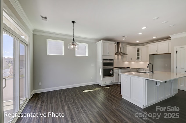 kitchen featuring a sink, crown molding, wall chimney exhaust hood, dark wood-type flooring, and light countertops
