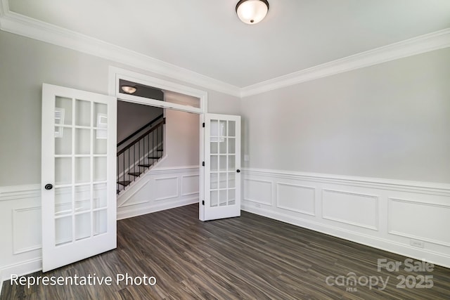 spare room featuring french doors, ornamental molding, a wainscoted wall, dark wood finished floors, and a decorative wall