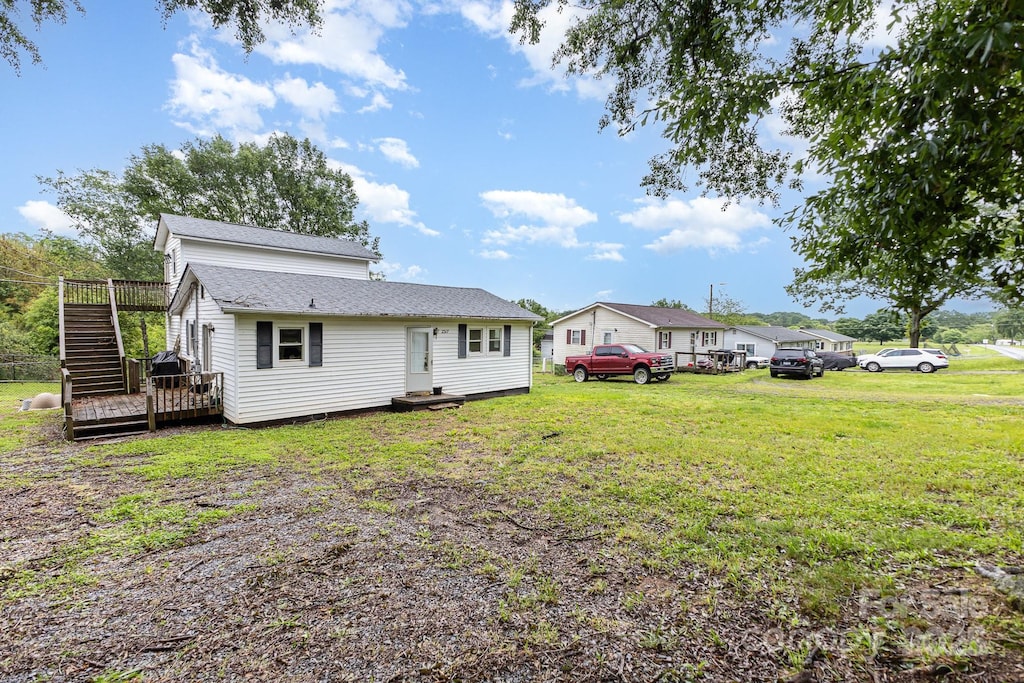 rear view of property featuring a yard, a deck, roof with shingles, and stairway