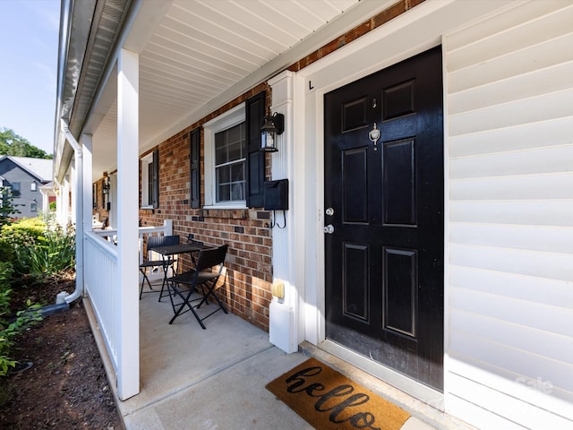 entrance to property featuring a porch and brick siding