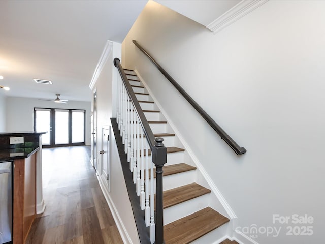 stairs with wood finished floors, a ceiling fan, crown molding, and baseboards