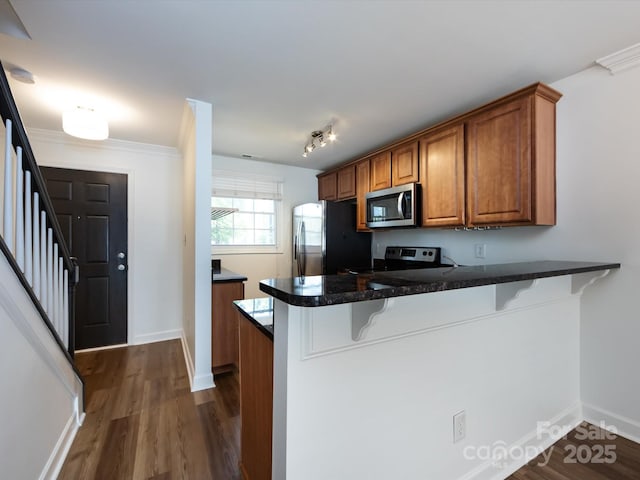 kitchen featuring appliances with stainless steel finishes, a breakfast bar area, brown cabinets, a peninsula, and dark wood finished floors