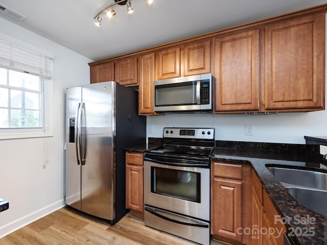 kitchen featuring appliances with stainless steel finishes, brown cabinets, a sink, light wood-style floors, and baseboards