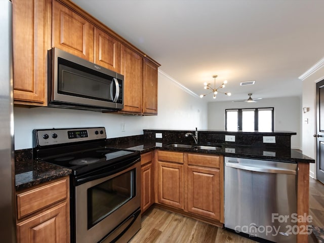 kitchen with appliances with stainless steel finishes, a sink, crown molding, a peninsula, and brown cabinetry