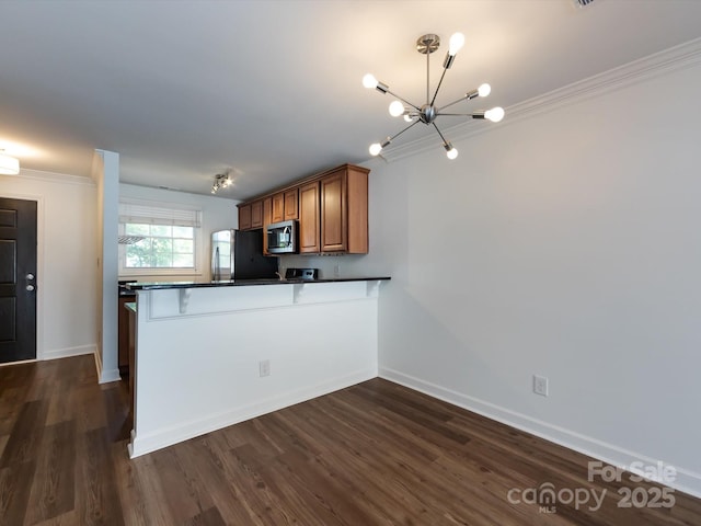kitchen with appliances with stainless steel finishes, dark countertops, brown cabinetry, a chandelier, and a peninsula