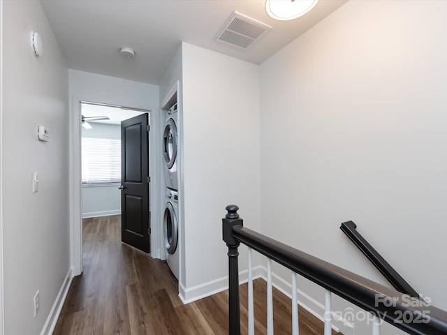 laundry area with stacked washer / drying machine, dark wood finished floors, and baseboards