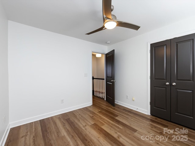 unfurnished bedroom featuring wood finished floors, baseboards, a closet, and a ceiling fan
