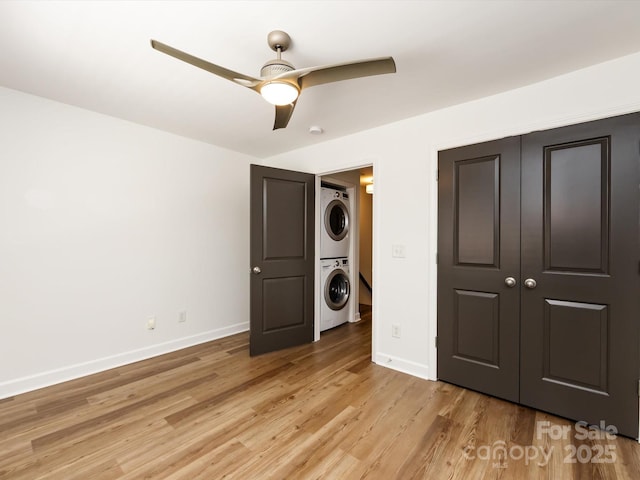 washroom with stacked washer and clothes dryer, ceiling fan, baseboards, and light wood-type flooring