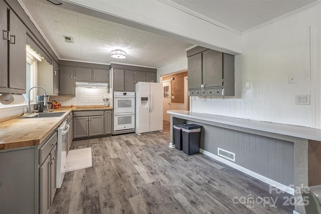 kitchen featuring white appliances, gray cabinetry, a sink, butcher block countertops, and wood finished floors