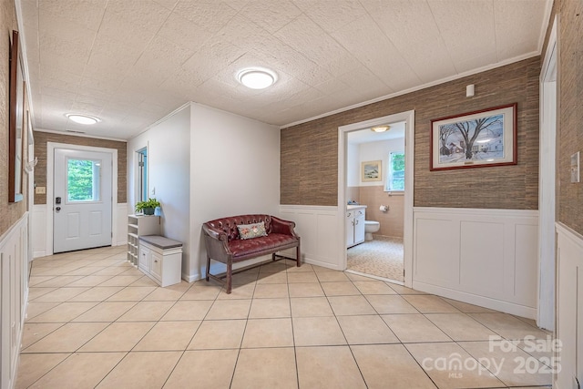 hallway featuring wainscoting, crown molding, and light tile patterned flooring