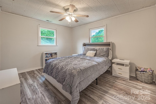 bedroom featuring multiple windows, wood finished floors, a ceiling fan, baseboards, and ornamental molding