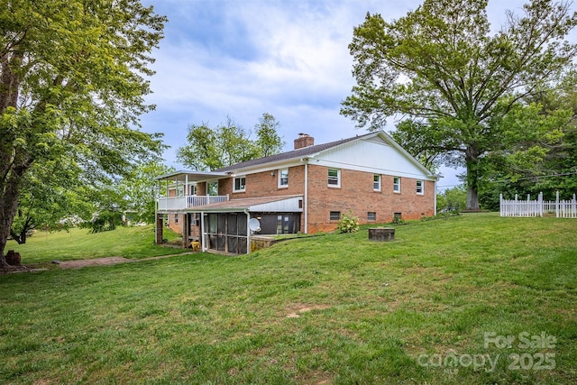 rear view of property with a sunroom, a chimney, brick siding, and a lawn