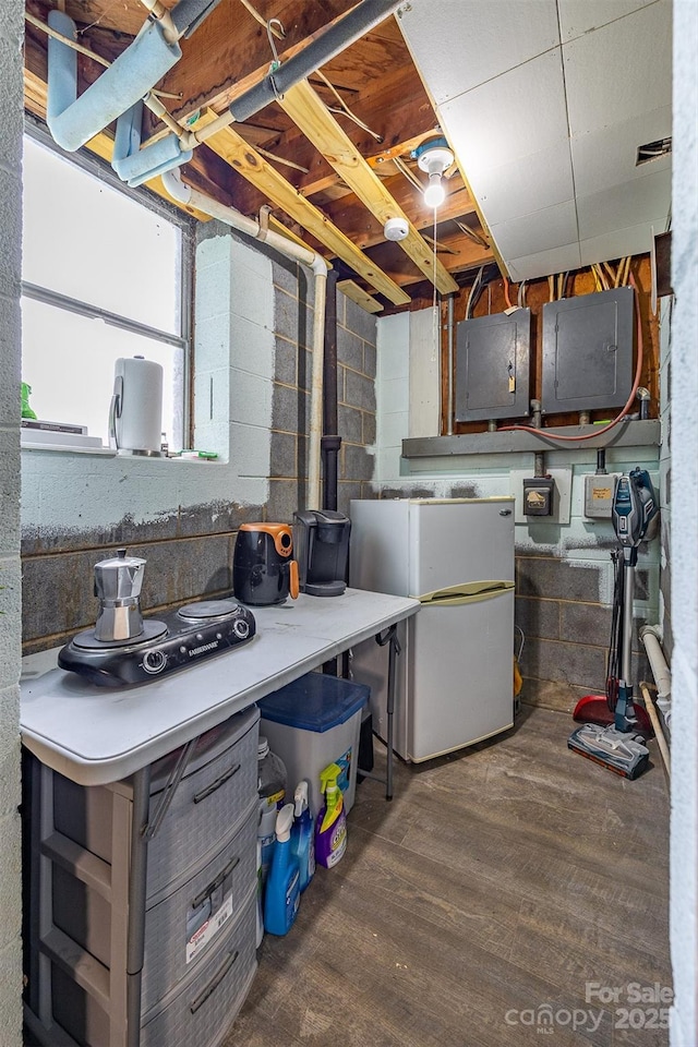 below grade area featuring freestanding refrigerator, electric panel, wood finished floors, and concrete block wall