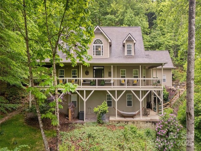 back of house with central air condition unit, a wooded view, stairway, a shingled roof, and a patio area