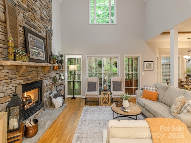 living area with a stone fireplace, hardwood / wood-style floors, a towering ceiling, and a chandelier