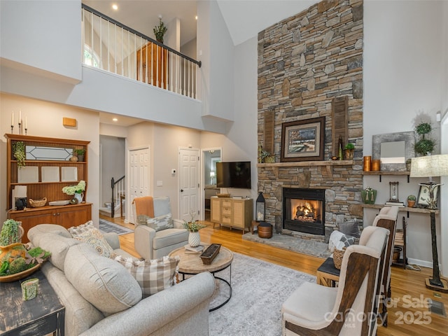 living room with stairway, wood finished floors, a stone fireplace, and a towering ceiling