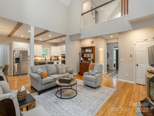 living area with light wood finished floors, decorative columns, a towering ceiling, baseboards, and recessed lighting