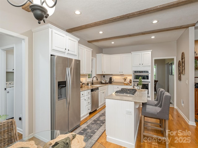kitchen with appliances with stainless steel finishes, a sink, white cabinetry, beamed ceiling, and a kitchen island