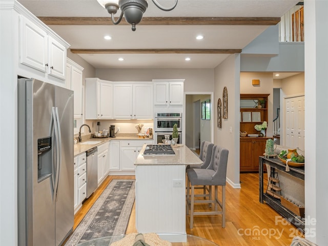 kitchen with stainless steel appliances, a sink, beamed ceiling, light wood-type flooring, and white cabinetry