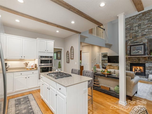 kitchen featuring stainless steel appliances, beamed ceiling, open floor plan, a stone fireplace, and a breakfast bar area