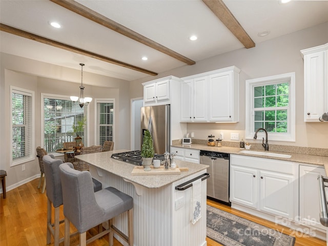kitchen featuring appliances with stainless steel finishes, a sink, beamed ceiling, white cabinets, and a chandelier
