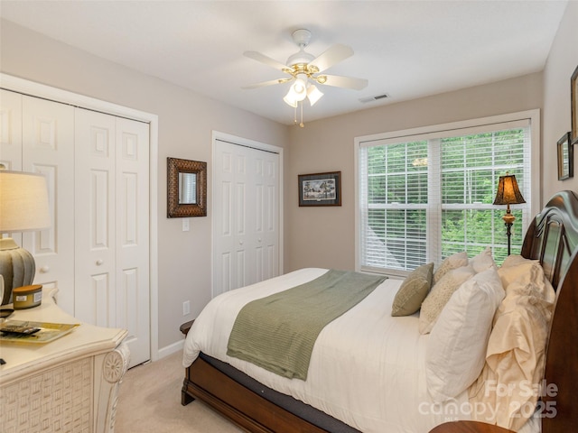 bedroom with two closets, light colored carpet, a ceiling fan, and baseboards