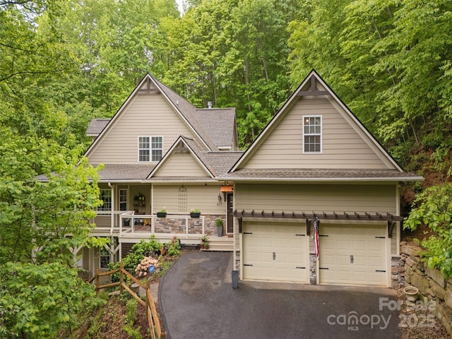 view of front of house with a garage, driveway, a shingled roof, and a porch